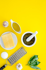 Make pesto sauce. Cheese, garlic, green basil, olive oil, salt near grater and mortar on yellow background top view copy space