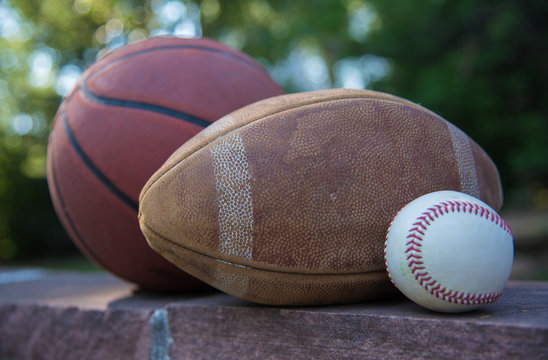 A Basketball, Football And Baseball Sit On A Ledge