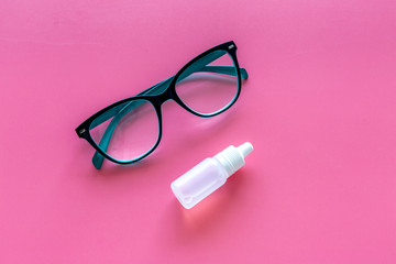 Eye drops in small bottle near glasses on pink background top view copy space