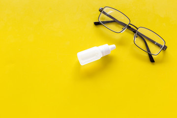 Eye drops in small bottle near glasses on yellow background top view copy space