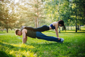 Young girl and guy doing push-ups in the park on the lawn. Doing sports outdoors. People in sportswear do exercises