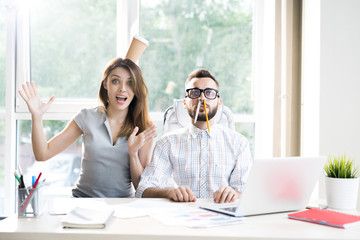 Portrait of two modern business people goofing around having fun while looking at camera sitting at...