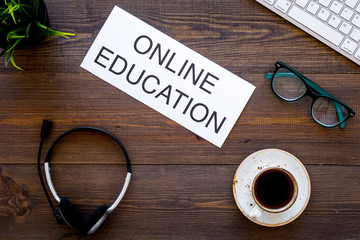Online learning concept. Words online education on dark wooden office work desk with computer keyboard, headphones, plant, glasses and coffee top view