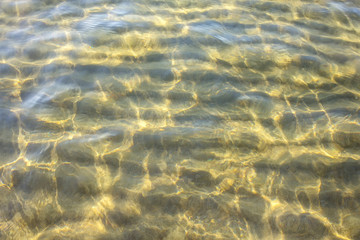 Fototapeta na wymiar Sandy seabed through transparent sea water . Crystal clear waters background
