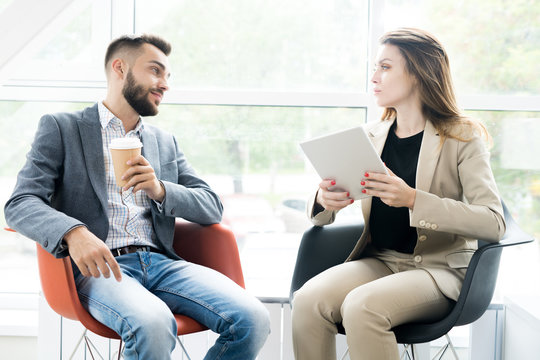 Portrait Of Two Modern Business People, Man And Woman, Sitting In Designer Chairs And Talking To Each Other In Sunlit Room