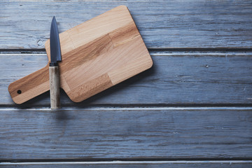 Wooden chopping board and knife on a rustic wood plank background