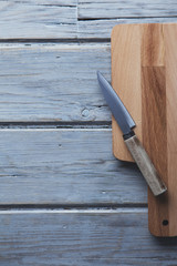 Wooden chopping board and knife on a rustic wood plank background