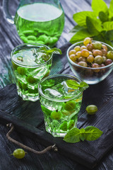 green gooseberry cocktail with ice and fresh mint on a black wooden table