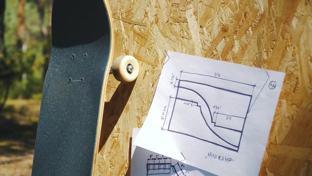 view of a new skateboard on a wooden background with plans for a miniramp in a skatepark in the summer