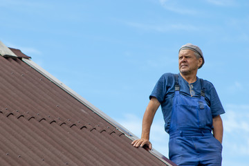 Old man working, building a roof of a house without any safety devices, wearing work clothes, blue...