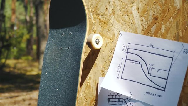view of a new skateboard on a wooden background with plans for a miniramp in a skatepark in the summer