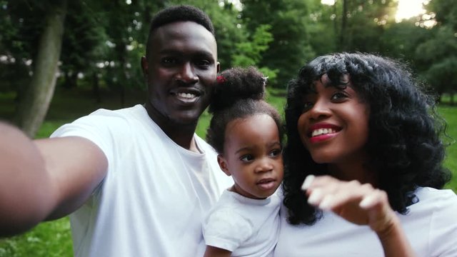 Smiling african american family having fun in the park pose to take a selfie slow motion happy smile close up child girl daughter couple summer nature picnic mother parents portrait