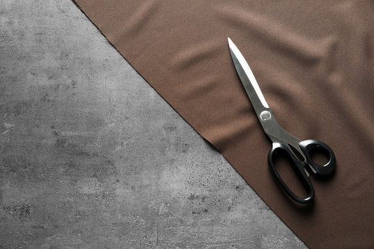 Scissors and fabric on grey background, top view. Tailoring equipment