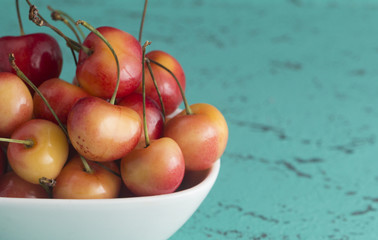 Bowl of Yellow and Red Cherries on a Teal Background