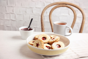 Traditional Christmas Linzer cookies with sweet jam and cup of tea on table
