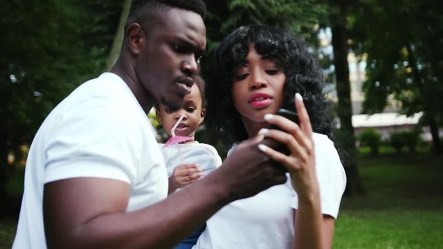 Serious african american man use phone with family standing wife and daughter slow motion close up child girl couple summer nature picnic mother parents portrait