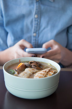 food, technology, eating and people concept - woman sitting at cafe table with smartphone and bowl of vegetable chicken soup 