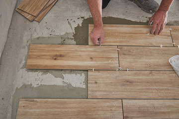 Hands of the tiler are laying the ceramic wood effect tiles on the floor