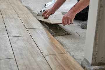 Laying wood effect tiles on the floor. Worker laying floor tiles.