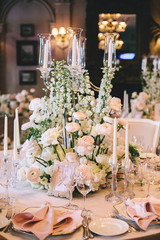 A beautifully designed banquet table with floral composition of buttercups and white roses, old porcelain plates, decorative candlesticks, cutlery, wine glasses and pink napkin