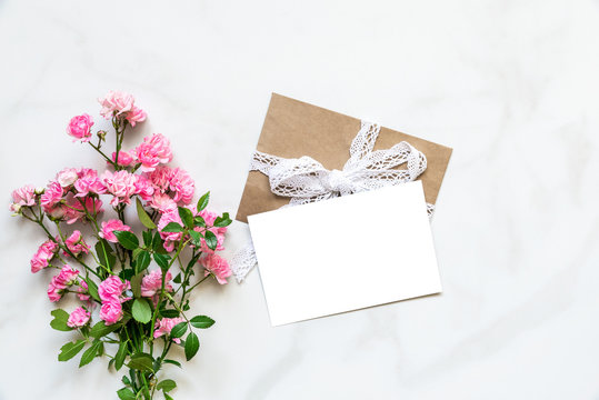 blank white greeting card with pink rose flowers bouquet over white marble table with copy space. top view