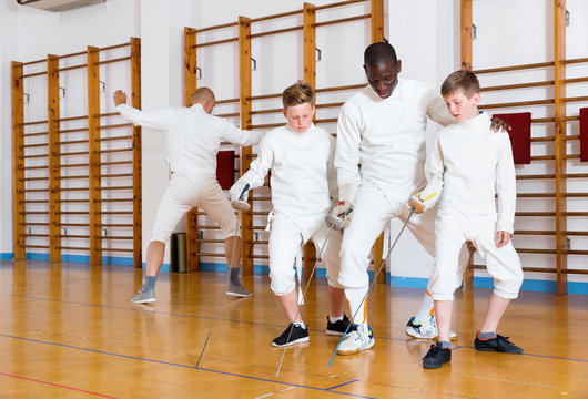 Focused boys fencers attentively listening to professional fencing coach in gym