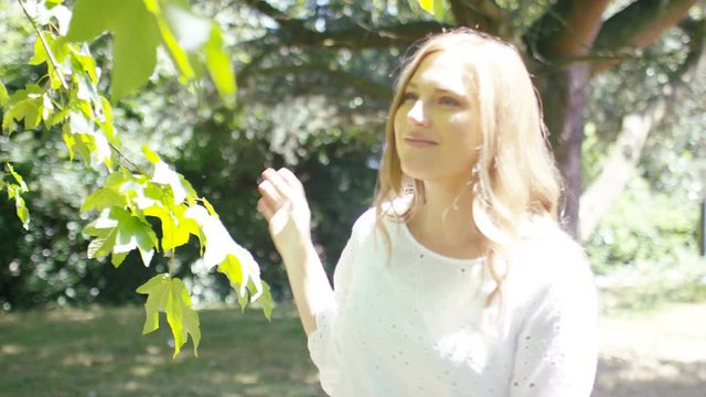 Young female walking through gardens in the sunlight, in slow motion