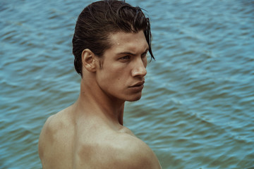 Strong face sport sexy male model on the sea shore background with sand and water on the beach on the sunset