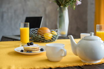 close up view of pancakes, cups of tea and glasses of juice for breakfast on table with yellow tablecloth