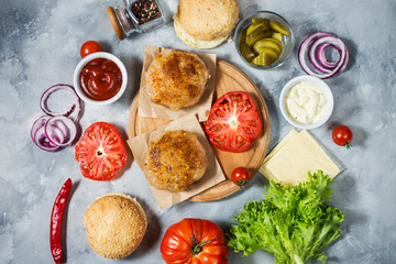 Ingredients for cooking burger. Grilled chicken patty, buns, onion, tomatoes, pickles, sauce, cheese over concrete background