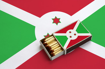 Burundi flag  is shown in an open matchbox, which is filled with matches and lies on a large flag