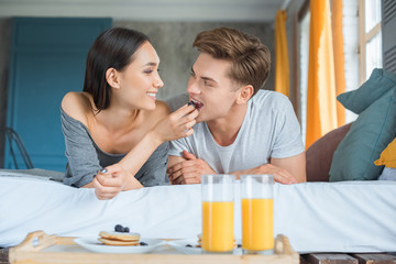 portrait of asian woman feeding caucasian boyfriend with breakfast in bed at home
