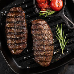 Closeup ready to eat steak Top Blade beef breeds of black Angus with grill tomato, garlic and on a wooden Board. The finished dish for dinner on a dark stone background. Top view