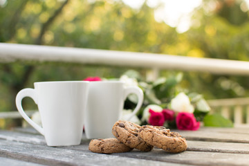 Chocolate chip cookies with two cups of coffee and flowers in the background