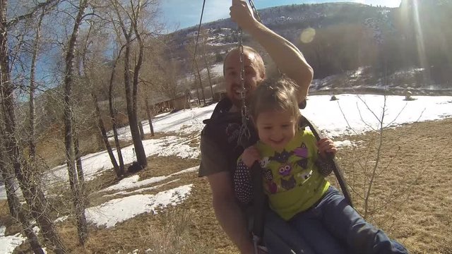 Father and daughter go down a zip line together, Zip line is set in back yard of a mountain cabin its springtime so some snow is still on the ground.