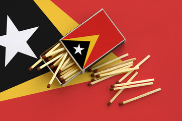 Timor Leste flag  is shown on an open matchbox, from which several matches fall and lies on a large...