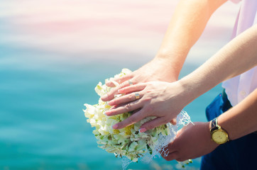 Close-up Bride and groom's hands with wedding rings and bouquet. Love and marriage. Wedding accessories and decor on the background of the river