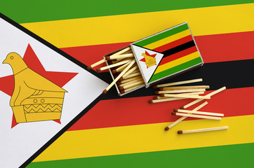 Zimbabwe flag  is shown on an open matchbox, from which several matches fall and lies on a large...