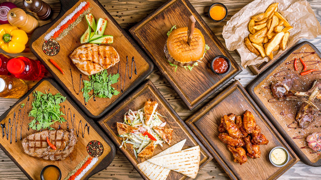 Assorted Meat Dishes. Burger, Fried Chicken Breast, Rib Eye Steak, Chicken Salad, Chicken Wings, Potatoes In The Country And A Rack Of Lamb On A Wooden Table