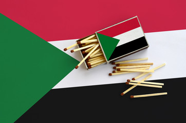 Sudan flag  is shown on an open matchbox, from which several matches fall and lies on a large flag