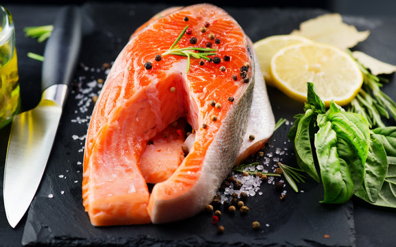 Salmon. Raw trout fish steak with herbs and lemon on black slate background. Cooking, seafood. Healthy eating concept