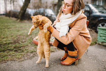 beautiful girl in a coat with a cat outdoors. portrait of a young woman outdoors