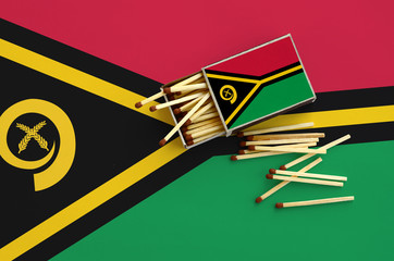 Vanuatu flag  is shown on an open matchbox, from which several matches fall and lies on a large flag