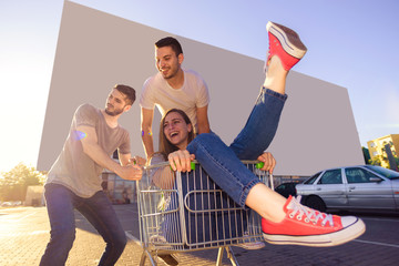 Young beautiful friends fooling around with a shopping trolley. Young and careless concept.