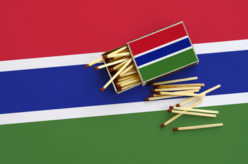 Gambia flag  is shown on an open matchbox, from which several matches fall and lies on a large flag