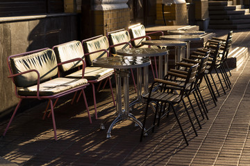 tables with sofas and chairs near the cafe one the street in the rays of sunlight