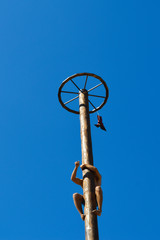 Fototapeta premium Boy climbing up on wooden slippery column to take the red woman boots at national Ukrainian annual market 