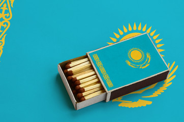 Kazakhstan flag  is shown in an open matchbox, which is filled with matches and lies on a large flag