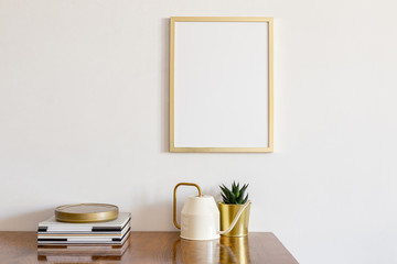 Golden frame over cabinet with golden flower pot and watering can on white wall. Minimal design. Mock up