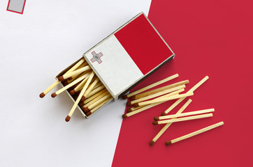 Malta flag  is shown on an open matchbox, from which several matches fall and lies on a large flag